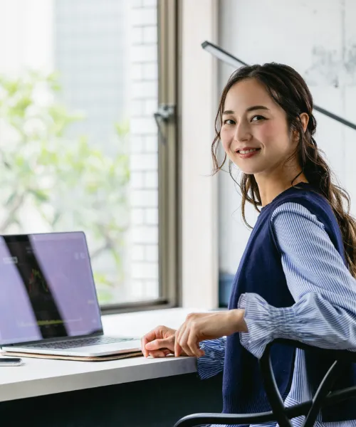 オフィスでノートパソコンを前に座り、こちらを振り返って微笑む人物の様子