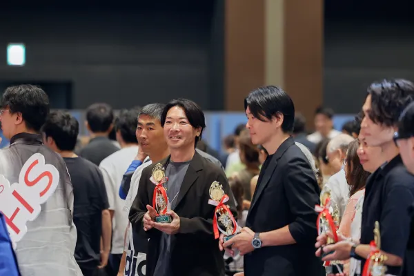 AI関連イベントの会場で、表彰トロフィーを手にした参加者が並んで立っている様子