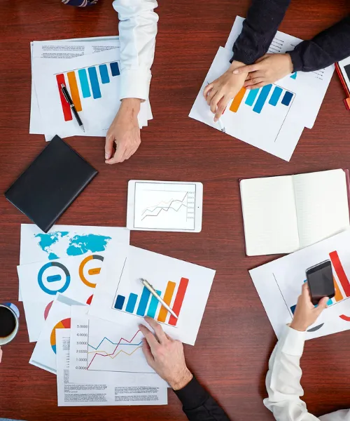 会議テーブルの上に並んだ資料やグラフを囲んで複数人が打ち合わせをしている様子