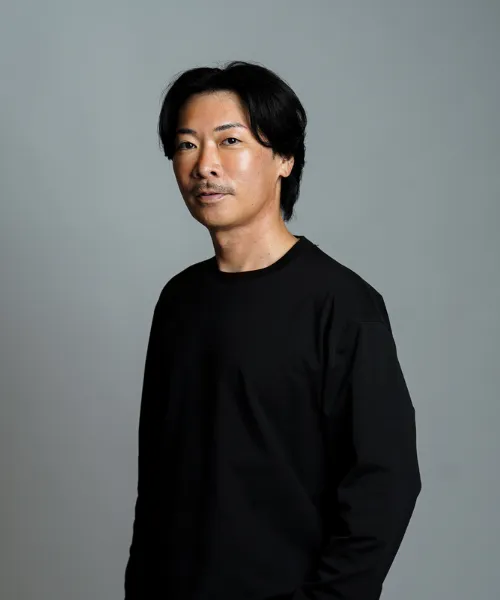 無地の背景の前に立つ人物を横から捉えたポートレート写真