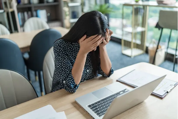 デスクでノートパソコンを前に、手で顔を覆って座っている人物の様子